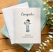 Graduation card with a cartoon graduate on a wooden surface with greenery