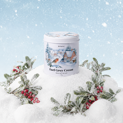 A tin of Rindos Earl Grey Cream tea sits in a snowy winter scene, surrounded by frosted holly leaves and red berries against a light blue snowy background.