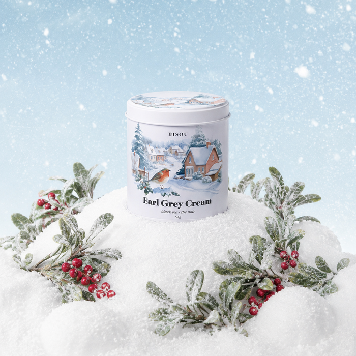 A tin of Rindos Earl Grey Cream tea sits in a snowy winter scene, surrounded by frosted holly leaves and red berries against a light blue snowy background.