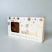 A rectangular box of 'salted.' brand salted caramels with a clear window showing the brown caramel product inside, decorated with gold snowflakes and text on a light gray background.