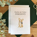 Birthday card with a corgi dog illustration and 'Happy Birthday CORGEOUS' text on a wooden surface with eucalyptus leaves and scissors.