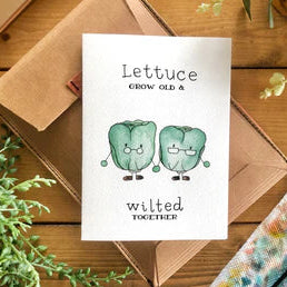 Anniversary Card with cartoon lettuce characters and text on a wooden surface with plants.