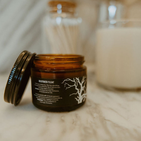 An open amber glass jar labeled 'BONDED ROAR' with a white tree graphic, placed on a marble surface with a white candle and other bathroom items blurred in the background.