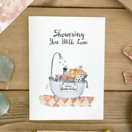 Greeting card with illustration of a bathtub and text 'Showering You with Love' on a wooden surface with decorative items.