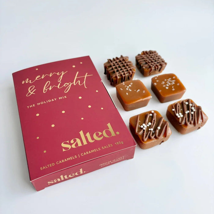 A red box of 'salted.' brand holiday salted caramels with gold foil lettering, shown next to five individually wrapped caramel candies on a clean white background.