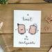 Newlywed Card with toast illustrations and text on a wooden surface with stationery items.
