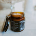 An amber glass jar of Nutri Fruitti body butter with its lid off, resting on a light marble surface with a softly blurred background.